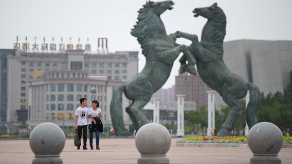 A photo taken on August 18, 2012 shows a couple walking past a statue in Genghis Khan Plaza, in the inner Mongolian city of Ordos - Sputnik International