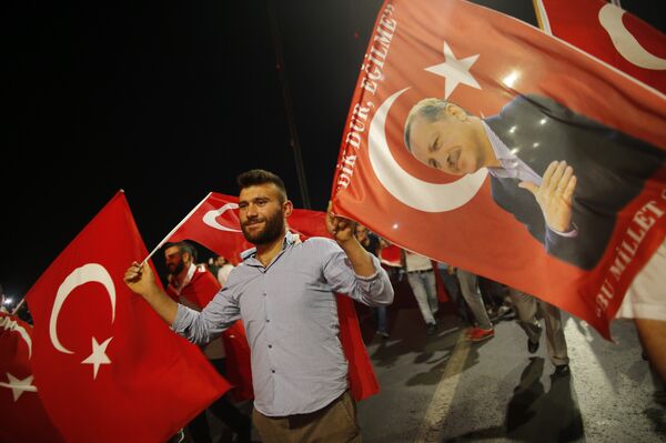 A pro-government supporter waves a Turkish flag and one with the picture of Turkey's President Recep Tayyip Erdogan, right, during a rally on the road leading to Istanbul's iconic Bosporus Bridge, Thursday, July 21, 2016 - Sputnik International