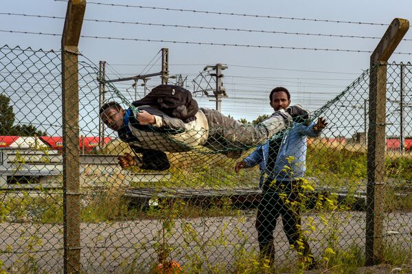 A migrant climbs over a fence in Coquelles, near Calais northern France A migrant climbs over a fence in Coquelles, near Calais northern France - Sputnik International