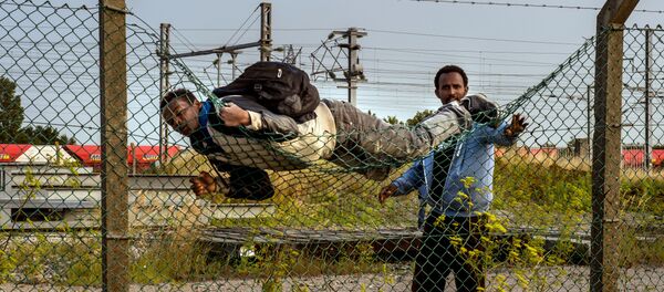 A migrant climbs over a fence in Coquelles, near Calais northern France - Sputnik International