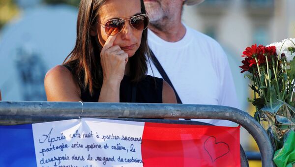 A woman reacts near flowers and flags placed in tribute to victims, two days after an attack by the driver of a heavy truck who ran into a crowd on Bastille Day killing scores and injuring as many on the Promenade des Anglais, in Nice, France, July 16, 2016. - Sputnik International