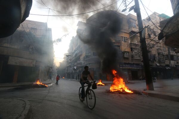 A man rides a bicycle past burning tyres, which activists said are used to create smoke cover from warplanes, in Aleppo, Syria August 1, 2016 - Sputnik International