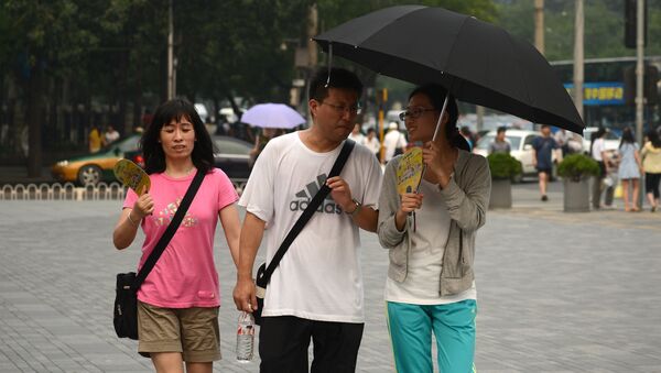 A woman holds an umbrella over herself and a man to shield against the hot weather conditions in Beijing. (File) - Sputnik International