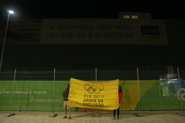 Protesters with a flag reading “Rio 2016: the Games of exclusion” stand under an official Rio Olympics’ banner reading, “The Olympics brings more than only the Olympics.” - Sputnik International