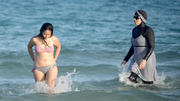 Tunisian women, one (R) wearing a burkini, a full-body swimsuit designed for Muslim women, swim on August 16, 2016 at Ghar El Melh beach near Bizerte, north-east of the capital Tunis. - Sputnik International