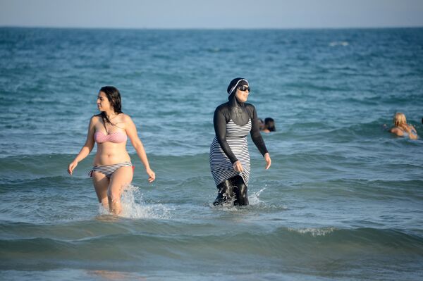 Tunisian women, one (R) wearing a burkini, a full-body swimsuit designed for Muslim women, swim at Ghar El Melh beach near Bizerte, north-east of the capital Tunis Tunisian women, one (R) wearing a burkini, a full-body swimsuit designed for Muslim women, swim at Ghar El Melh beach near Bizerte, north-east of the capital Tunis - Sputnik International