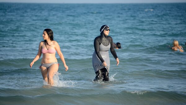 Tunisian women, one (R) wearing a burkini, a full-body swimsuit designed for Muslim women, swim at Ghar El Melh beach near Bizerte, north-east of the capital Tunis - Sputnik International