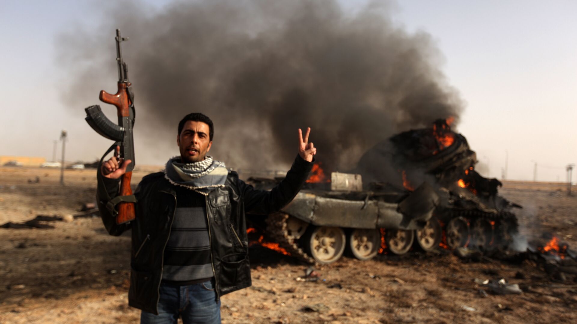 A Libyan rebel flashes a V-sign in front of burning tank belonging to loyalist forces bombed by coalition air force in the town of Ajdabiya on March 26, 2011 - Sputnik International, 1920, 15.02.2021