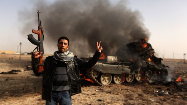 A Libyan rebel flashes a V-sign in front of burning tank belonging to loyalist forces bombed by coalition air force in the town of Ajdabiya on March 26, 2011 - Sputnik International