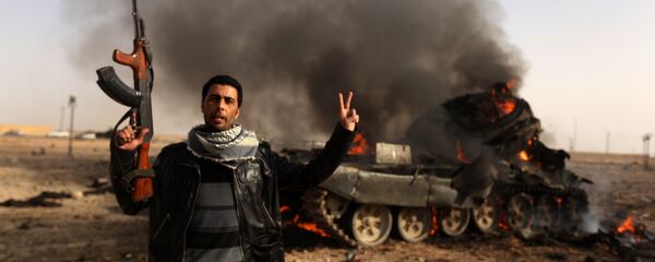 A Libyan rebel flashes a V-sign in front of burning tank belonging to loyalist forces bombed by coalition air force in the town of Ajdabiya on March 26, 2011 A Libyan rebel flashes a V-sign in front of burning tank belonging to loyalist forces bombed by coalition air force in the town of Ajdabiya on March 26, 2011 - Sputnik International