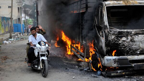 Men ride a motorcycle past a lorry in Bengaluru, which was set on fire by protesters after India's Supreme Court ordered Karnataka state to release 12,000 cubic feet of water per second every day from the Cauvery river to neighbouring Tamil Nadu, India September 12, 2016. - Sputnik International