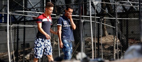 A migrant (R) reacts as he walks next to the remains of burned tents at the Moria migrant camp, after a fire that ripped through tents and destroyed containers during violence among residents, on the island of Lesbos, Greece, September 20, 2016. A migrant (R) reacts as he walks next to the remains of burned tents at the Moria migrant camp, after a fire that ripped through tents and destroyed containers during violence among residents, on the island of Lesbos, Greece, September 20, 2016. - Sputnik International