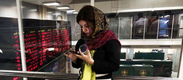 An Iranian woman uses a mobile phone next to a stock market activity board at the stock exchange in the capital Tehran on July 27, 2015 - Sputnik International