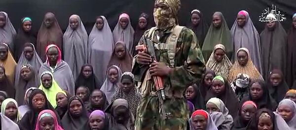This file photo taken on August 14, 2016 shows a video grab image created on August 14, 2016 and taken from a video released on youtube purportedly by Islamist group Boko Haram showing what is claimed to be one of the groups fighters at an undisclosed location standing in front of girls allegedly kidnapped from Chibok in April 2014. - Sputnik International