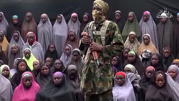 This file photo taken on August 14, 2016 shows a video grab image created on August 14, 2016 and taken from a video released on youtube purportedly by Islamist group Boko Haram showing what is claimed to be one of the groups fighters at an undisclosed location standing in front of girls allegedly kidnapped from Chibok in April 2014. - Sputnik International
