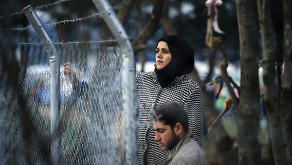 A couple stands behind a fence as refugees and migrants wait to cross the Greek-Macedonian border near the town of Gevgelija on March 3, 2016. - Sputnik International