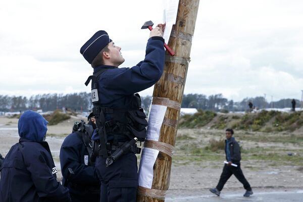 A French policeman posts the official document that announces the dismantling of the makeshift camp called the Jungle, as a migrant walks past in Calais, France, October 21, 2016 - Sputnik International