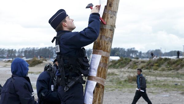 A French policeman posts the official document that announces the dismantling of the makeshift camp called the Jungle, as a migrant walks past in Calais, France, October 21, 2016 - Sputnik International