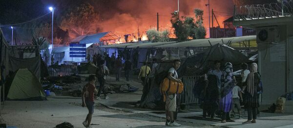 Migrants hold their belonging as a large fire burns inside the Moria refugee camp on the northeastern Greek island of Lesbos, late Monday, Sept. 19. 2016 - Sputnik International