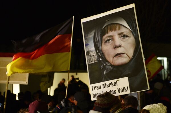 A protestor holds a poster with an image of German Chancellor Angela Merkel wearing a headscarf in front of the Reichstag building with a crescent on top during a rally of the group Patriotic Europeans against the Islamization of the West, or PEGIDA, in Dresden, Germany, Monday, Jan. 12, 2015 A protestor holds a poster with an image of German Chancellor Angela Merkel wearing a headscarf in front of the Reichstag building with a crescent on top during a rally of the group Patriotic Europeans against the Islamization of the West, or PEGIDA, in Dresden, Germany, Monday, Jan. 12, 2015 - Sputnik International