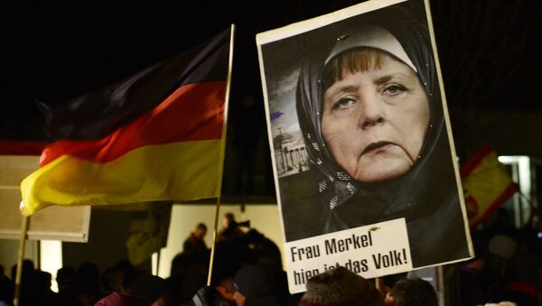 A protestor holds a poster with an image of German Chancellor Angela Merkel wearing a headscarf in front of the Reichstag building with a crescent on top during a rally of the group Patriotic Europeans against the Islamization of the West, or PEGIDA, in Dresden, Germany, Monday, Jan. 12, 2015 - Sputnik International
