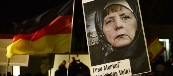 A protestor holds a poster with an image of German Chancellor Angela Merkel wearing a headscarf in front of the Reichstag building with a crescent on top during a rally of the group Patriotic Europeans against the Islamization of the West, or PEGIDA, in Dresden, Germany, Monday, Jan. 12, 2015 A protestor holds a poster with an image of German Chancellor Angela Merkel wearing a headscarf in front of the Reichstag building with a crescent on top during a rally of the group Patriotic Europeans against the Islamization of the West, or PEGIDA, in Dresden, Germany, Monday, Jan. 12, 2015 - Sputnik International