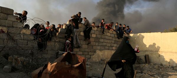 A newly displaced woman runs after she jumped over a back wall and rushed to grab humanitarian packages, as smoke rises from a burning oil refinery at a processing centre in Qayyara, south of Mosul, Iraq October 25, 2016 - Sputnik International