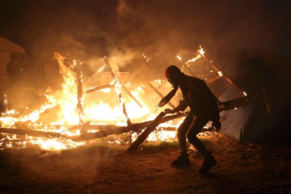 A migrant is seen in silhouette near flames from a burning makeshift shelter on the second day of the evacuation of migrants and their transfer to reception centers in France, as part of the dismantlement of the camp called the Jungle in Calais, France, October 25, 2016 A migrant is seen in silhouette near flames from a burning makeshift shelter on the second day of the evacuation of migrants and their transfer to reception centers in France, as part of the dismantlement of the camp called the Jungle in Calais, France, October 25, 2016 - Sputnik International
