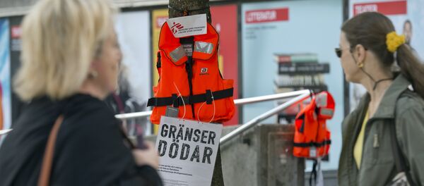 Women pass by a life vest and a placard reading Borders kill hanging on a tree in Stockholm as part of an action by Swedish branch of humanitarian NGO Doctors without borders, in solidarity with migrants seeking asylum in Europe after fleeing their home countries on September 14, 2015 Women pass by a life vest and a placard reading Borders kill hanging on a tree in Stockholm as part of an action by Swedish branch of humanitarian NGO Doctors without borders, in solidarity with migrants seeking asylum in Europe after fleeing their home countries on September 14, 2015 - Sputnik International