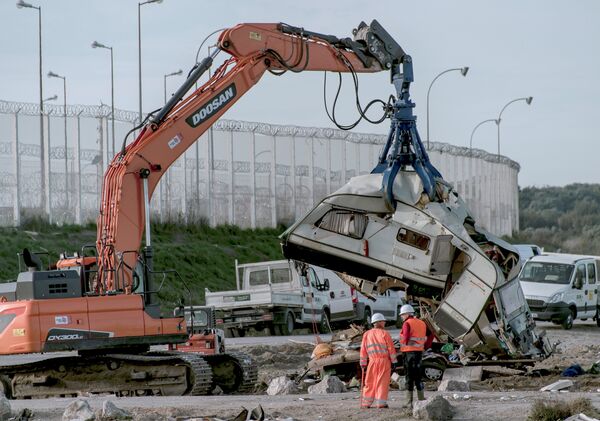 Workers watch as a crane destroys a caravan, once used as a makeshift shelter, at the site of the 'Jungle' migrant camp, on October 31, 2016 in Calais, northern France, as a massive operation to clear the settlement nears completion Workers watch as a crane destroys a caravan, once used as a makeshift shelter, at the site of the 'Jungle' migrant camp, on October 31, 2016 in Calais, northern France, as a massive operation to clear the settlement nears completion - Sputnik International
