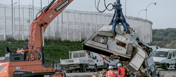 Workers watch as a crane destroys a caravan, once used as a makeshift shelter, at the site of the 'Jungle' migrant camp, on October 31, 2016 in Calais, northern France, as a massive operation to clear the settlement nears completion Workers watch as a crane destroys a caravan, once used as a makeshift shelter, at the site of the 'Jungle' migrant camp, on October 31, 2016 in Calais, northern France, as a massive operation to clear the settlement nears completion - Sputnik International