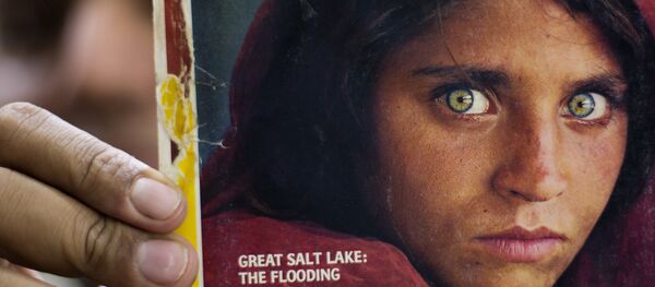 In this file photo taken on Wednesday, Oct. 26, 2016, Pakistan's Inam Khan, owner of a book shop shows a copy of a magazine with the photograph of Afghan refugee woman Sharbat Gulla In this file photo taken on Wednesday, Oct. 26, 2016, Pakistan's Inam Khan, owner of a book shop shows a copy of a magazine with the photograph of Afghan refugee woman Sharbat Gulla - Sputnik International