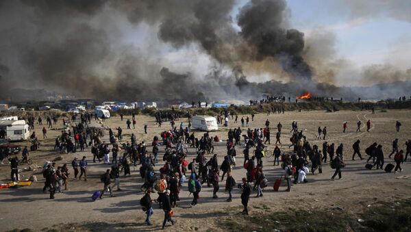 Oct. 26, 2016 file photo people walk past as thick smoke and flames rise from amidst the tents after fires were started in the makeshift migrant camp known as the jungle near Calais, northern France. - Sputnik International