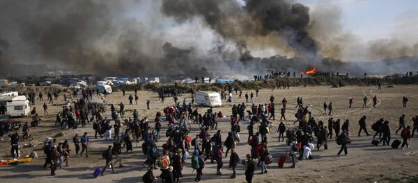 Oct. 26, 2016 file photo people walk past as thick smoke and flames rise from amidst the tents after fires were started in the makeshift migrant camp known as the jungle near Calais, northern France. - Sputnik International