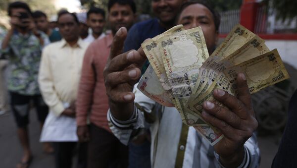 An Indian man displays Indian currency notes of 1000 and 500 rupees as he stands in queue to exchange or deposit discontinued currency notes outside a post office in Ahmadabad, India, Thursday, Nov. 10, 2016. - Sputnik International