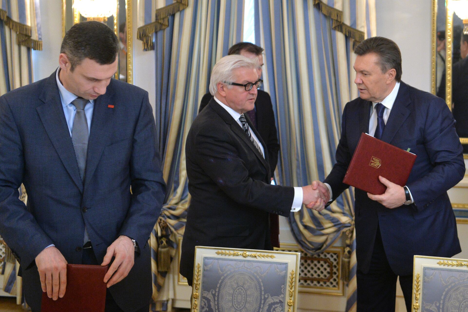 German Foreign Affairs minister Frank-Walter Steinmeier (C) and Ukrainian President Viktor Yanukovych (R) shake hands as head of Vitali Klitschko, one of Maidan's leaders, looks on after the signing of what was thought to be a compromise deal in Kiev on February 21, 2014 - Sputnik International, 1920, 25.02.2024