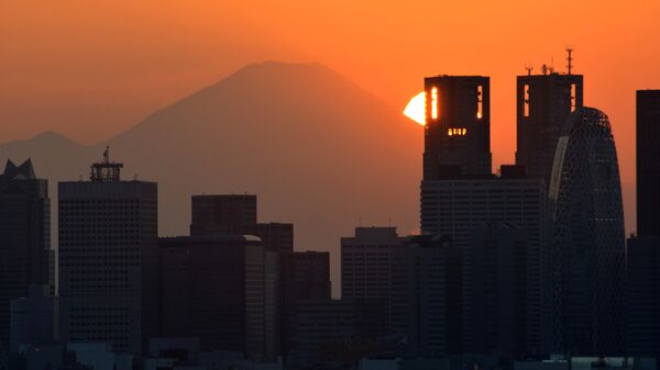 This picture taken on November 7, 2016 shows the sun setting behind the Japan's highest mountain Mount Fuji and skyscrapers in Tokyo's Shinjuku area. - Sputnik International