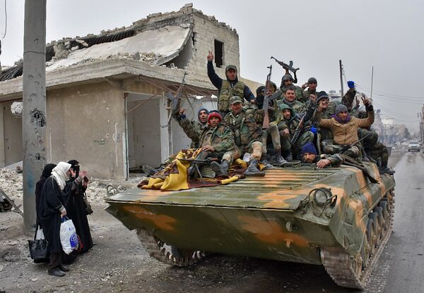 Syrian pro-government forces sit on a military vehicle driving past residents fleeing the eastern part of Aleppo and gathering in Masaken Hanano, a former rebel-held district which was retaken by the regime forces last week, on November 30, 2016. Syrian pro-government forces sit on a military vehicle driving past residents fleeing the eastern part of Aleppo and gathering in Masaken Hanano, a former rebel-held district which was retaken by the regime forces last week, on November 30, 2016. - Sputnik International
