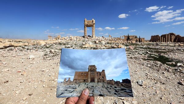 A general view taken on March 31, 2016 shows a photographer holding his picture of the Temple of Bel taken on March 14, 2014 in front of the remains of the historic temple after it was destroyed by Islamic State (IS) group jihadists in September 2015 in the ancient Syrian city of Palmyra - Sputnik International