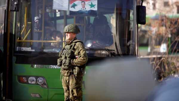 A Russian soldier stands near a bus carrying people who came back to inspect their homes in government controlled Hanono housing district in Aleppo, Syria December 4, 2016 - Sputnik International