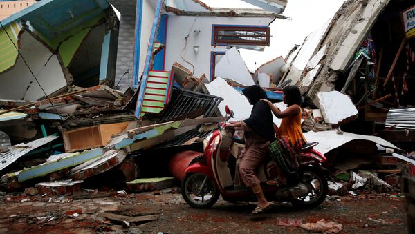 A woman and child ride a motorcycle past damaged buildings following this week's strong earthquake in Meureudu market, Pidie Jaya, Aceh province, Indonesia December 9, 2016. - Sputnik International