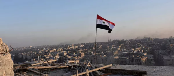 A Syrian national flag flutters near a general view of eastern Aleppo after Syrian government soldiers took control of al-Sakhour neigborhood in Aleppo, Syria in this handout picture provided by SANA on November 28, 2016. - Sputnik International