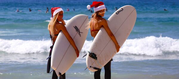 German tourists Mimi Wiebeling (L) and Pauline Lapetite carry surfboards as they walk into the surf wearing Christmas hats at Sydney's Bondi Beach on Christmas Day in Australia German tourists Mimi Wiebeling (L) and Pauline Lapetite carry surfboards as they walk into the surf wearing Christmas hats at Sydney's Bondi Beach on Christmas Day in Australia - Sputnik International