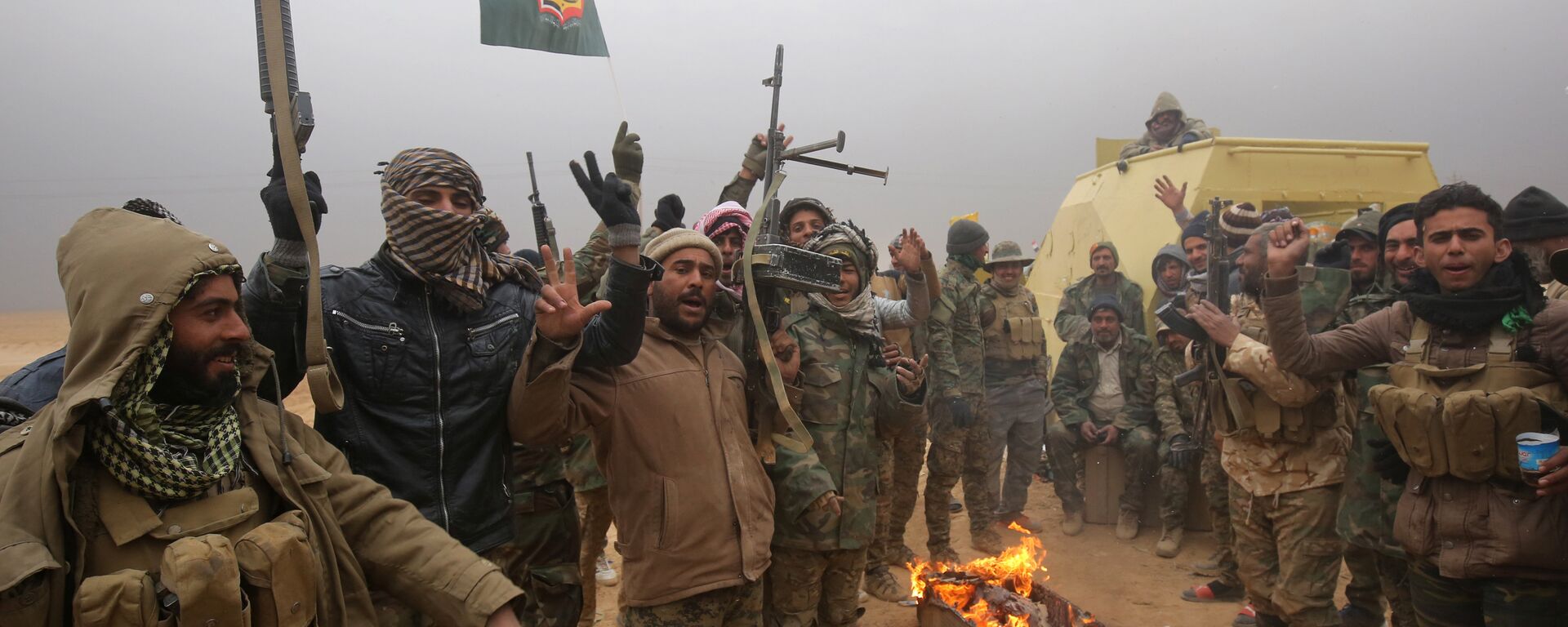Iraqi Shiite fighters from the Hashed al-Shaabi (Popular Mobilisation) paramilitaries gesture to the camera as they warm up around a fire near the village of Tal Faris, south of Tal Afar, on November 30, 2016, during a broad offencive by Iraq forces to retake the city Mosul from jihadists of the Islamic State group - Sputnik International, 1920, 26.10.2023