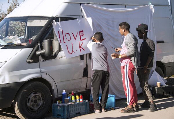 Young migrants paint a sheet of paper with the lettering 'I love UK' in the 'Jungle' migrant camp, in Calais, northern France, on October 31, 2016, during a massive operation to clear the squalid settlement where 6,000-8,000 people have been living in dire conditions. - Sputnik International