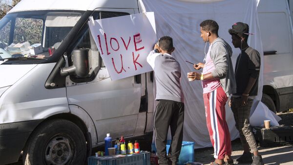 Young migrants paint a sheet of paper with the lettering 'I love UK' in the 'Jungle' migrant camp, in Calais, northern France, on October 31, 2016, during a massive operation to clear the squalid settlement where 6,000-8,000 people have been living in dire conditions - Sputnik International