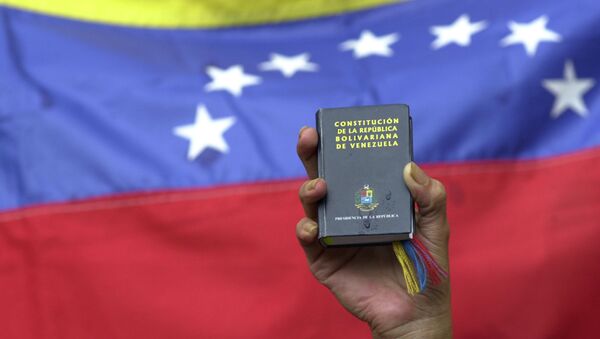 A demonstrator holds up a miniature copy of Venezuela's constitution in front of the nation's flag at a government rally in Caracas, Venezuela, Tuesday, April 13, 2004. - Sputnik International
