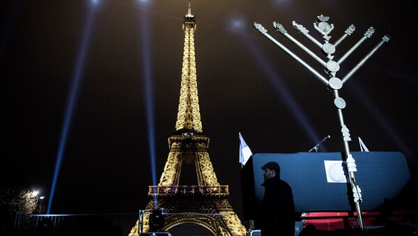 A member of the Jewish community stands near a Menorah (Hanukkah), a nine-branched candelabrum, before the lighting of two branches in front of the Eiffel tower in Paris on December 25, 2016. - Sputnik International