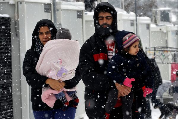 Stranded Syrian refugees carry their children through a snow storm at a refugee camp north of Athens, Greece January 10, 2017. - Sputnik International