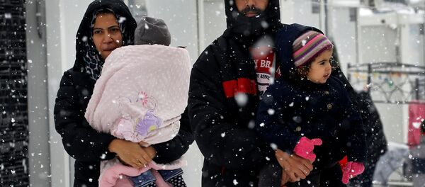 Stranded Syrian refugees carry their children through a snow storm at a refugee camp north of Athens, Greece January 10, 2017. - Sputnik International